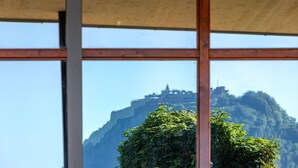 A view through a window with a metal frame, showcasing a mountain with a castle-like structure in the background.