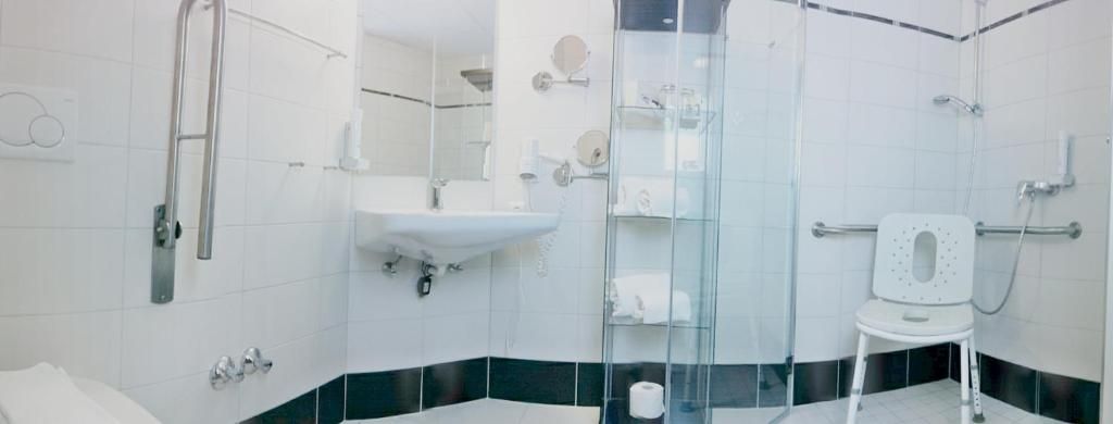 Un baño moderno con cabina de ducha de vidrio, un lavabo blanco y un inodoro con asiento de seguridad.