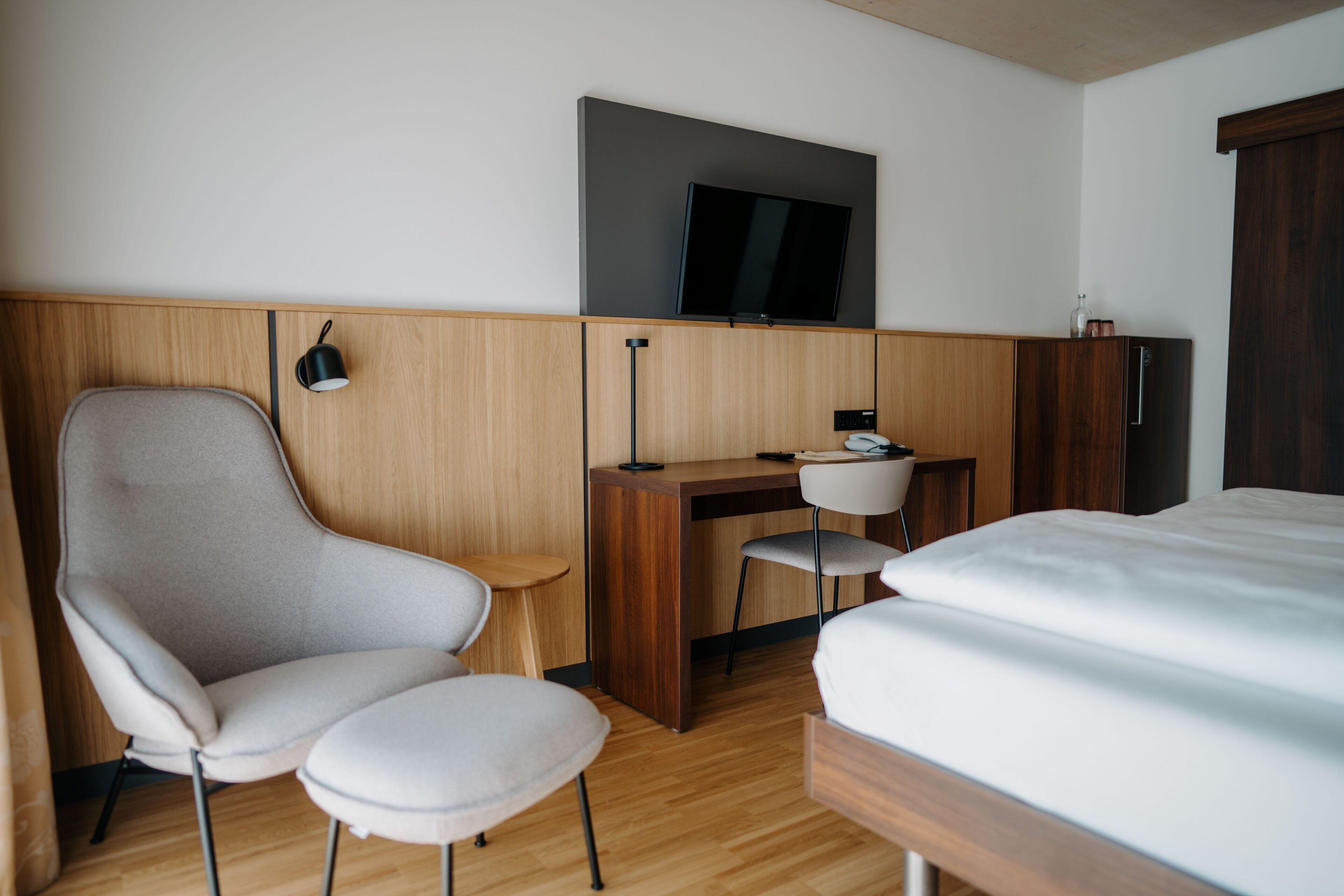 A hotel room with a bed, a desk, a chair, a television, and a wardrobe.