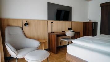 A hotel room with a bed, a desk, a chair, a television, and a wardrobe.