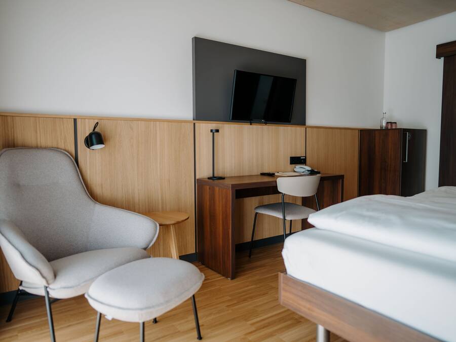A hotel room with a bed, a desk, a chair, a television, and a wardrobe.