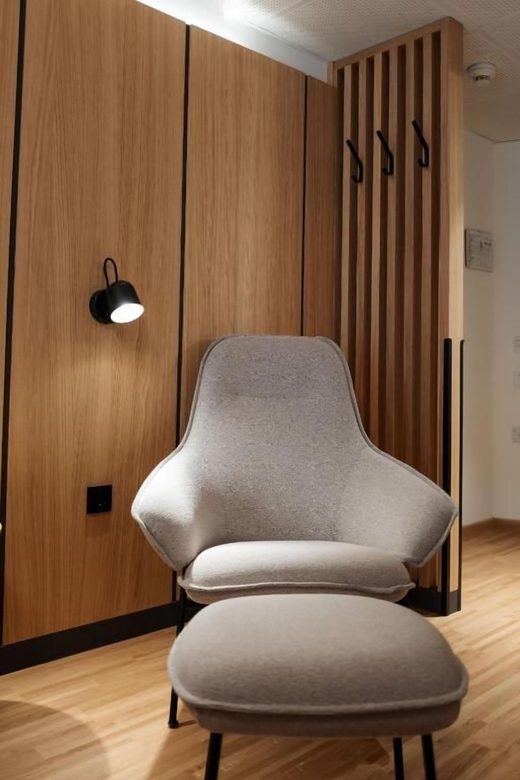 Una habitación moderna con un panel de pared de madera, un sillón tapizado color gris y una lámpara de pie negra.