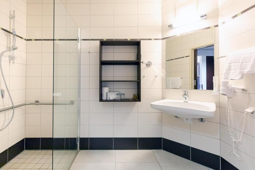 Un baño moderno con ducha envuelta en vidrio, un lavamanos blanco y un espejo sobre él.