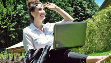 A person sitting on grass with a laptop, a bag, and a pair of shoes.