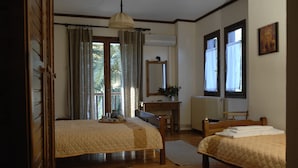 Quarto com duas camas, penteadeira de madeira, escrivaninha e janela com cortinas.