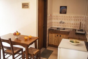 Une petite cuisine avec une table en bois, des chaises, un réfrigérateur, un évier et un plan de travail carrelé.