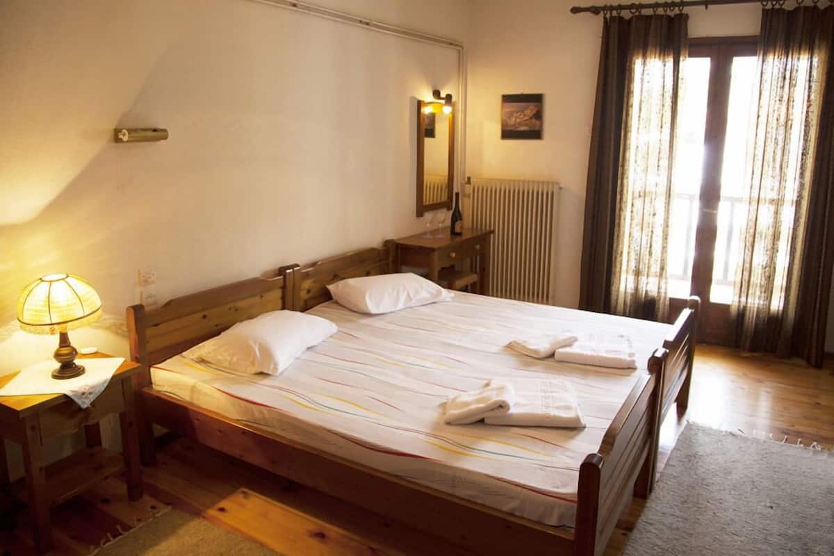 A neatly made bed with white linens and towels, a bedside lamp, a wooden nightstand, and a window with curtains.