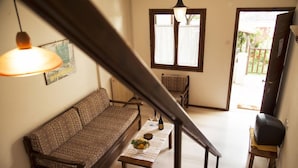 Uma sala de estar com um sofá, uma mesa de centro com uma tigela de frutas, uma garrafa de vinho e uma televisão em um suporte.