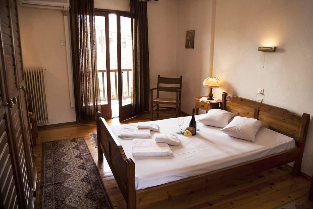 A neatly made bed with white linens and towels, a wooden nightstand with a lamp, a chair, and a radiator.