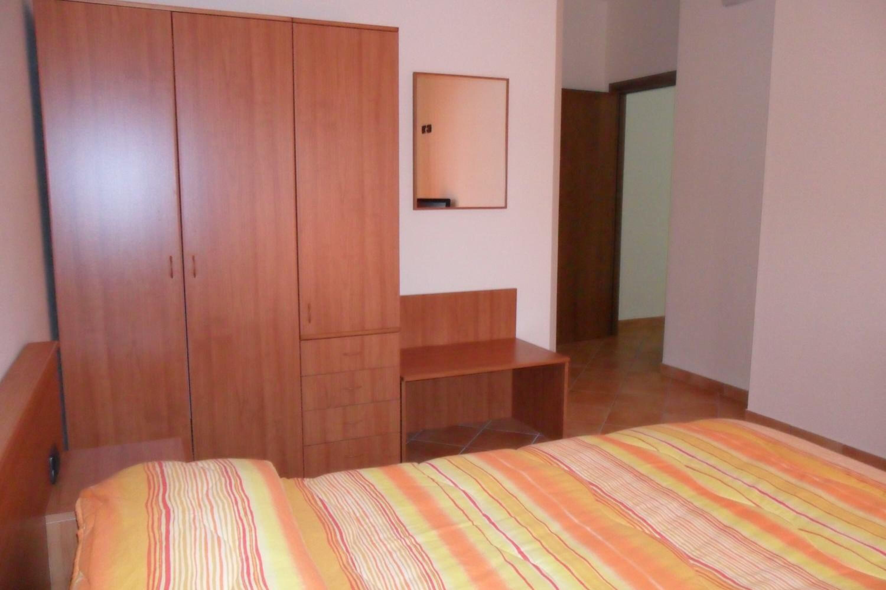 A bedroom with a bed, wooden wardrobe, and a mirror on the wall.