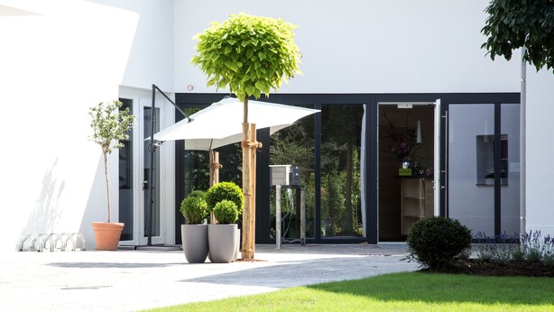 A modern building with a covered entrance, large potted plants, and a well-maintained lawn. - Villa Verde (Salzburg)