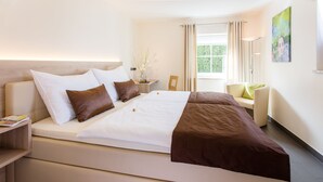 A modern hotel room with a large bed, a bedside table, a chair, and a window with curtains. - Villa Verde (Salzburg)