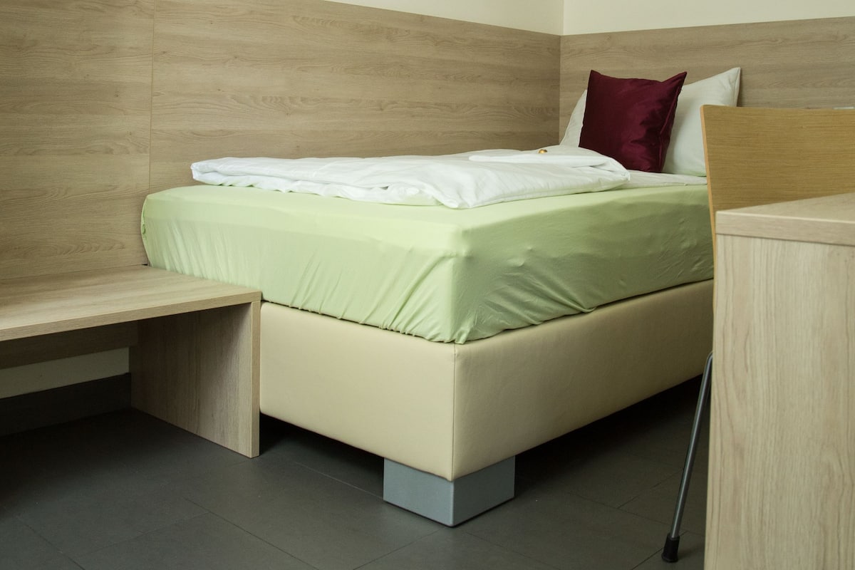 A modern bedroom with a bed, a wooden nightstand, and a desk.