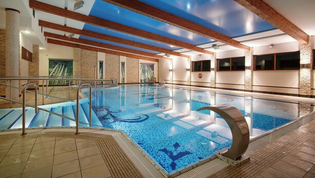 An indoor swimming pool with clear blue water, wooden beams on the ceiling, and a stone wall. - Artis Hotel & Spa (Zamosc)
