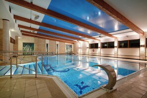 An indoor swimming pool with clear blue water, wooden beams on the ceiling, and a stone wall. - Artis Hotel & Spa (Zamosc)