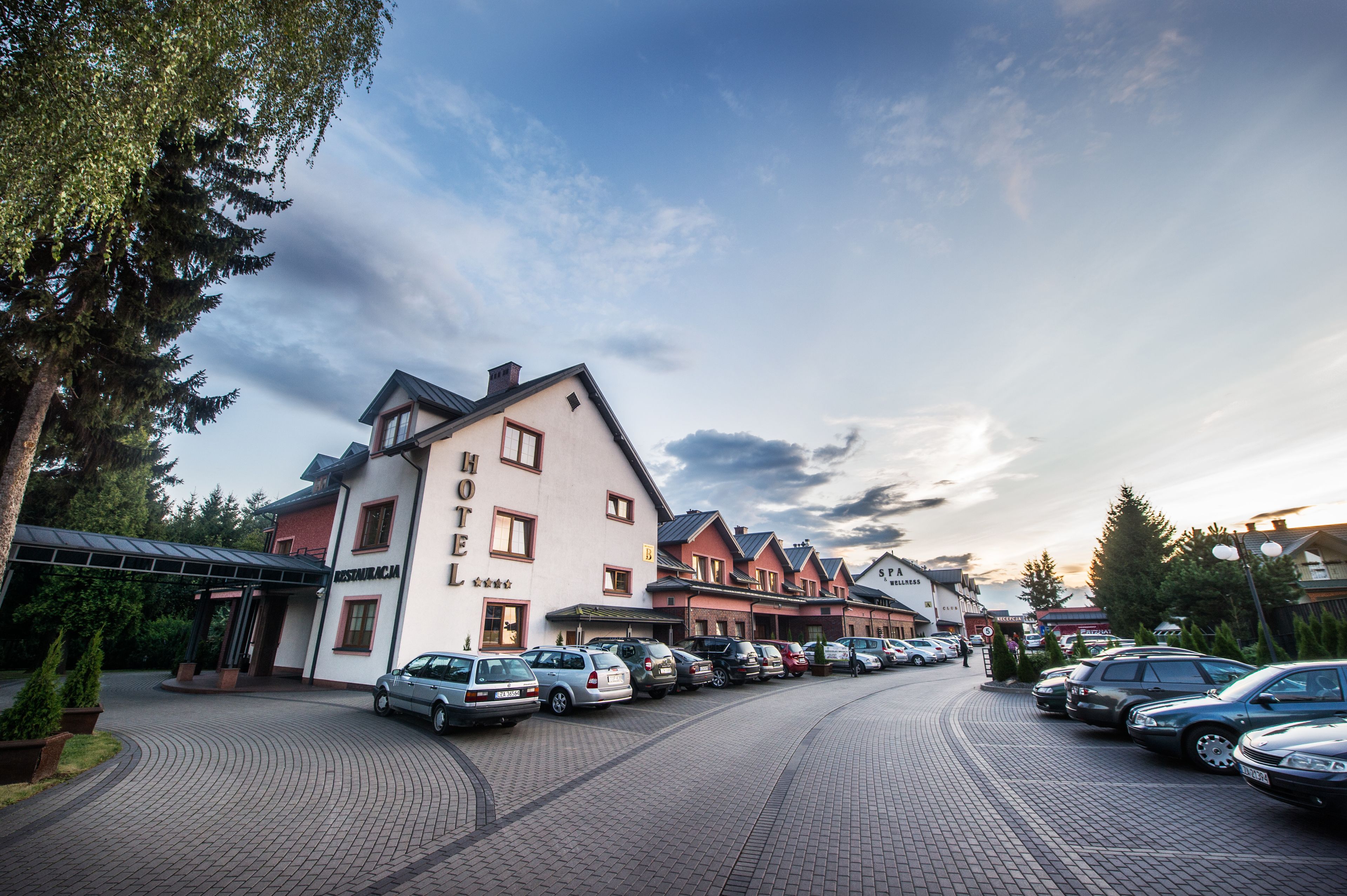 Et hotel med restaurant, flere parkerede biler og en asfalteret indkørsel.