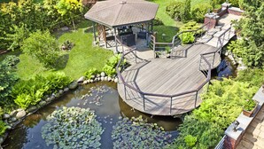 A gazebo with a wooden deck, surrounded by a pond with lily pads, and lush greenery. - Artis Hotel & Spa (Zamosc)