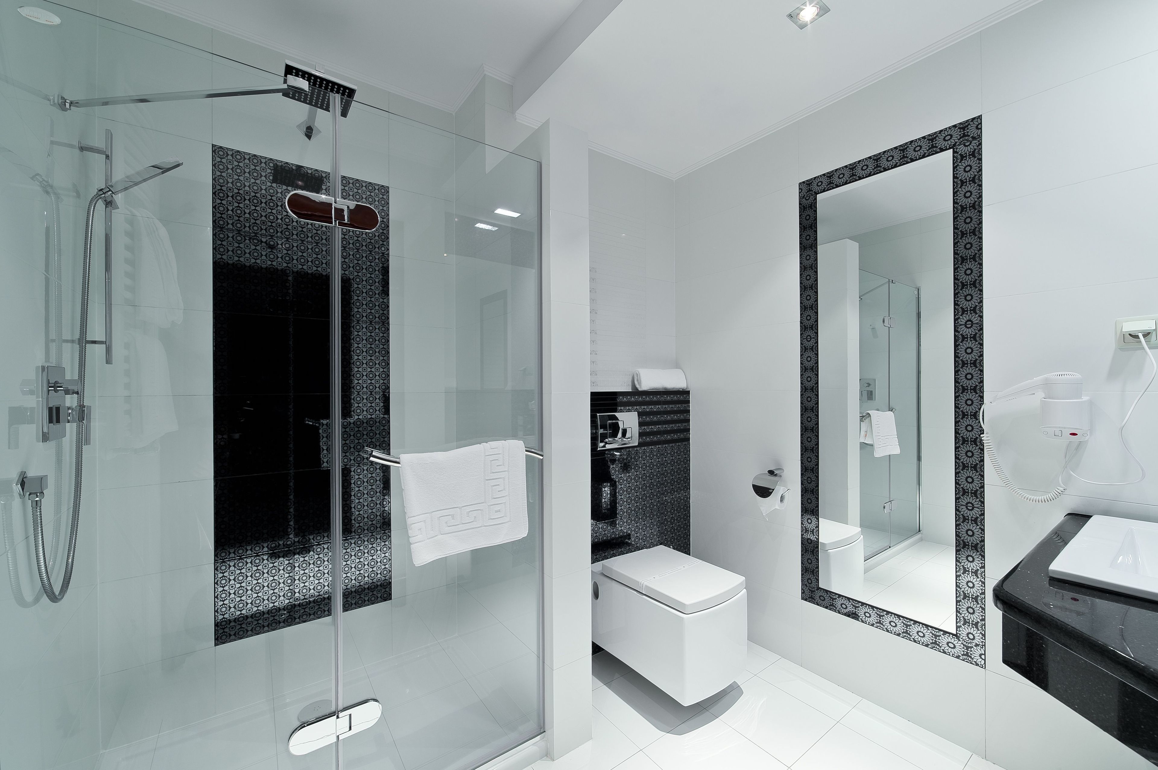 A modern bathroom with a glass-enclosed shower, a toilet, and a large mirror with a decorative frame.