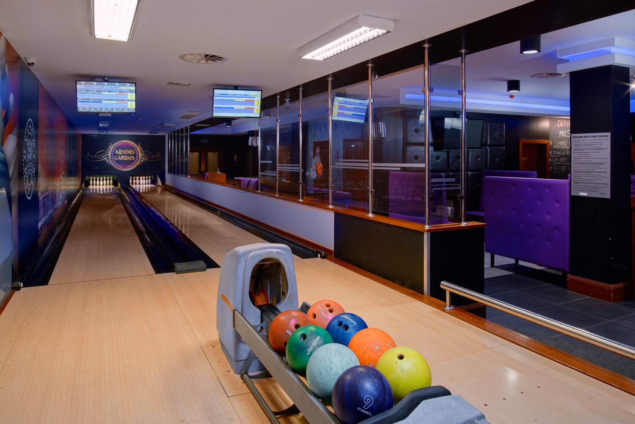 A bowling alley with a lane, bowling balls, and a scoreboard.