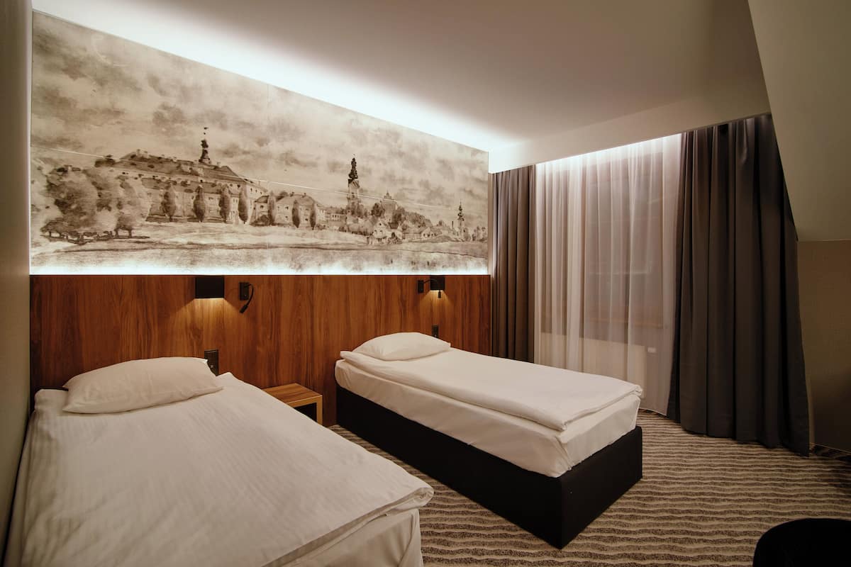 A hotel room with two beds, a large wall-mounted painting, wooden paneling, and a window with curtains.