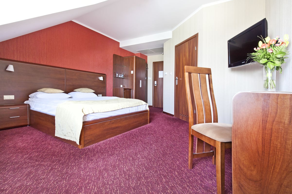 A hotel room with a bed, a desk, a chair, a TV, and a bouquet of flowers.