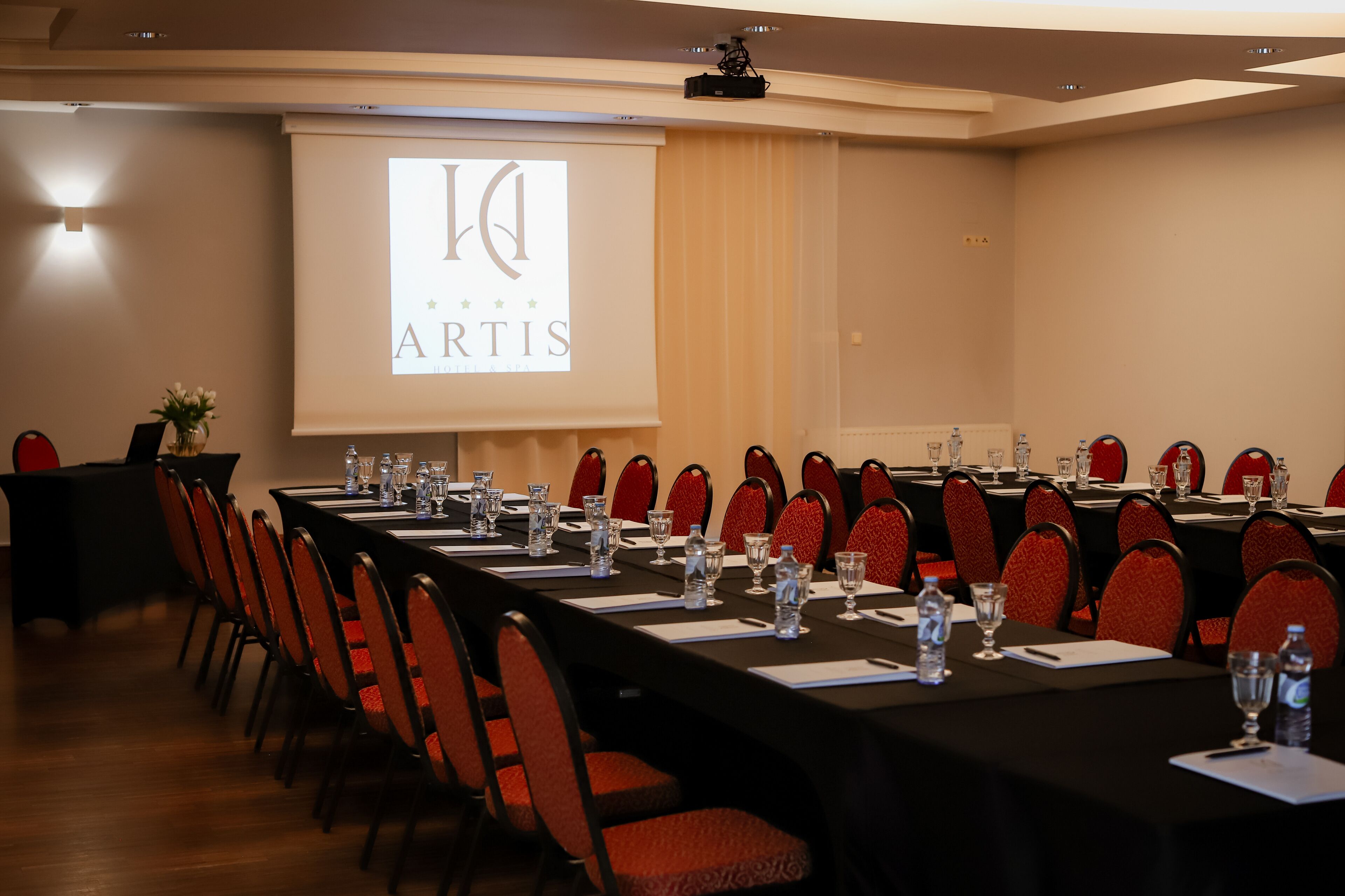 Ein Konferenzraum mit einem langen Tisch, roten Stühlen und einer Projektionsleinwand, die "ARTIS" zeigt.