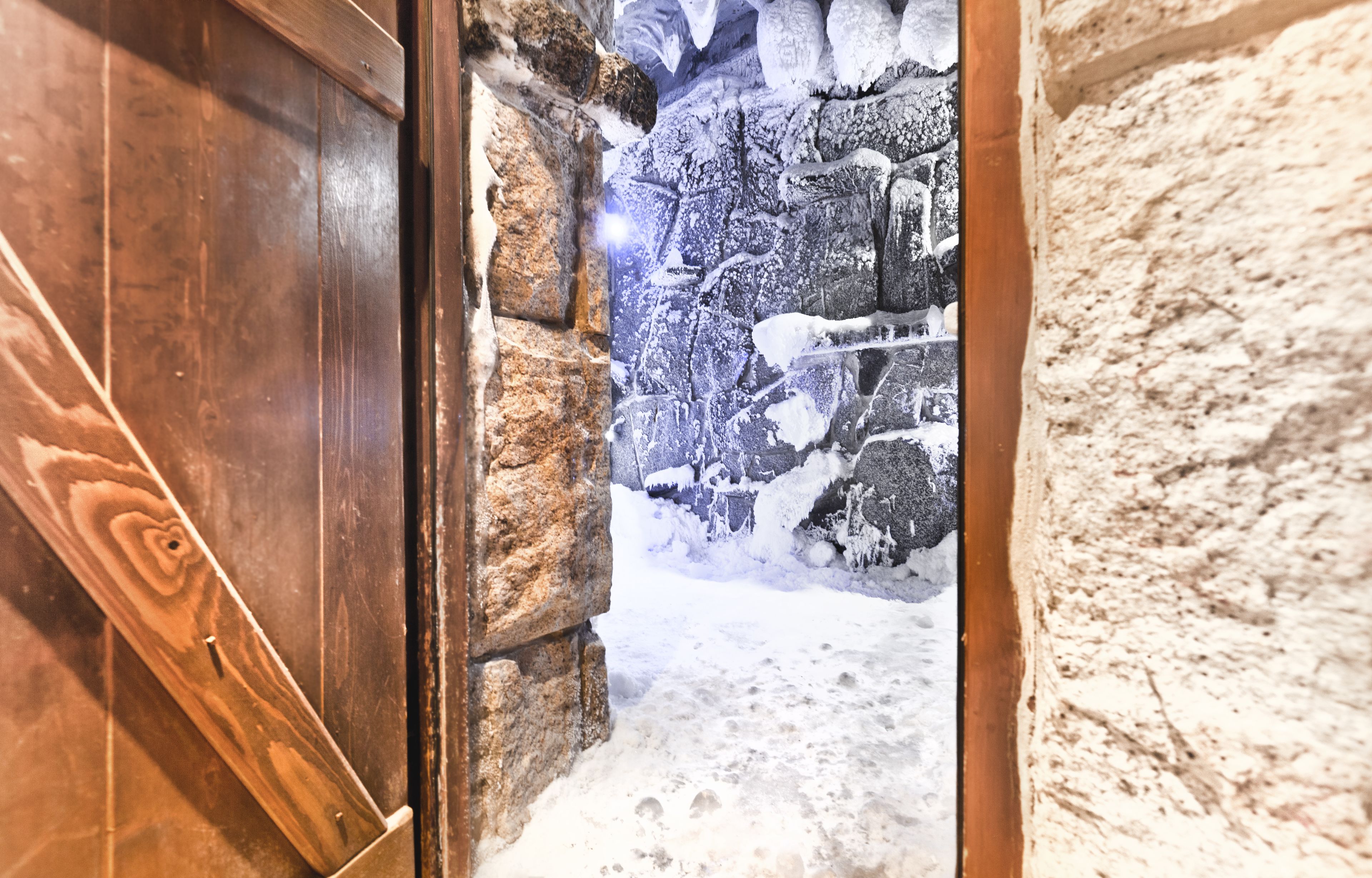 A stone wall with a wooden door leading to a snowy outdoor area.