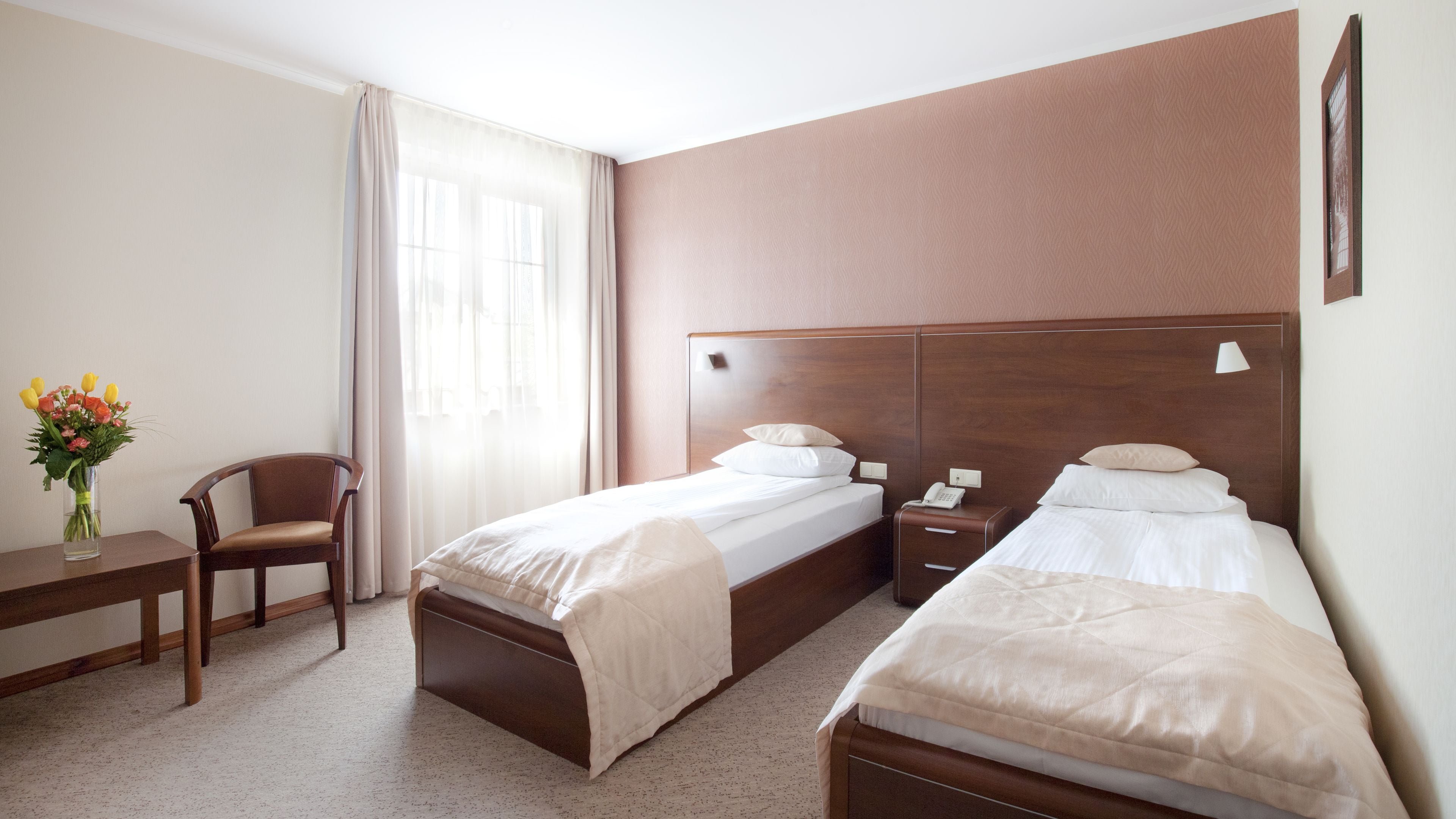 A hotel room with two beds, a desk, a chair, and a window with curtains.