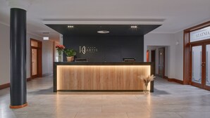 A hotel reception desk with a modern design, featuring a wooden counter and a logo above it. - Artis Hotel & Spa (Zamosc)