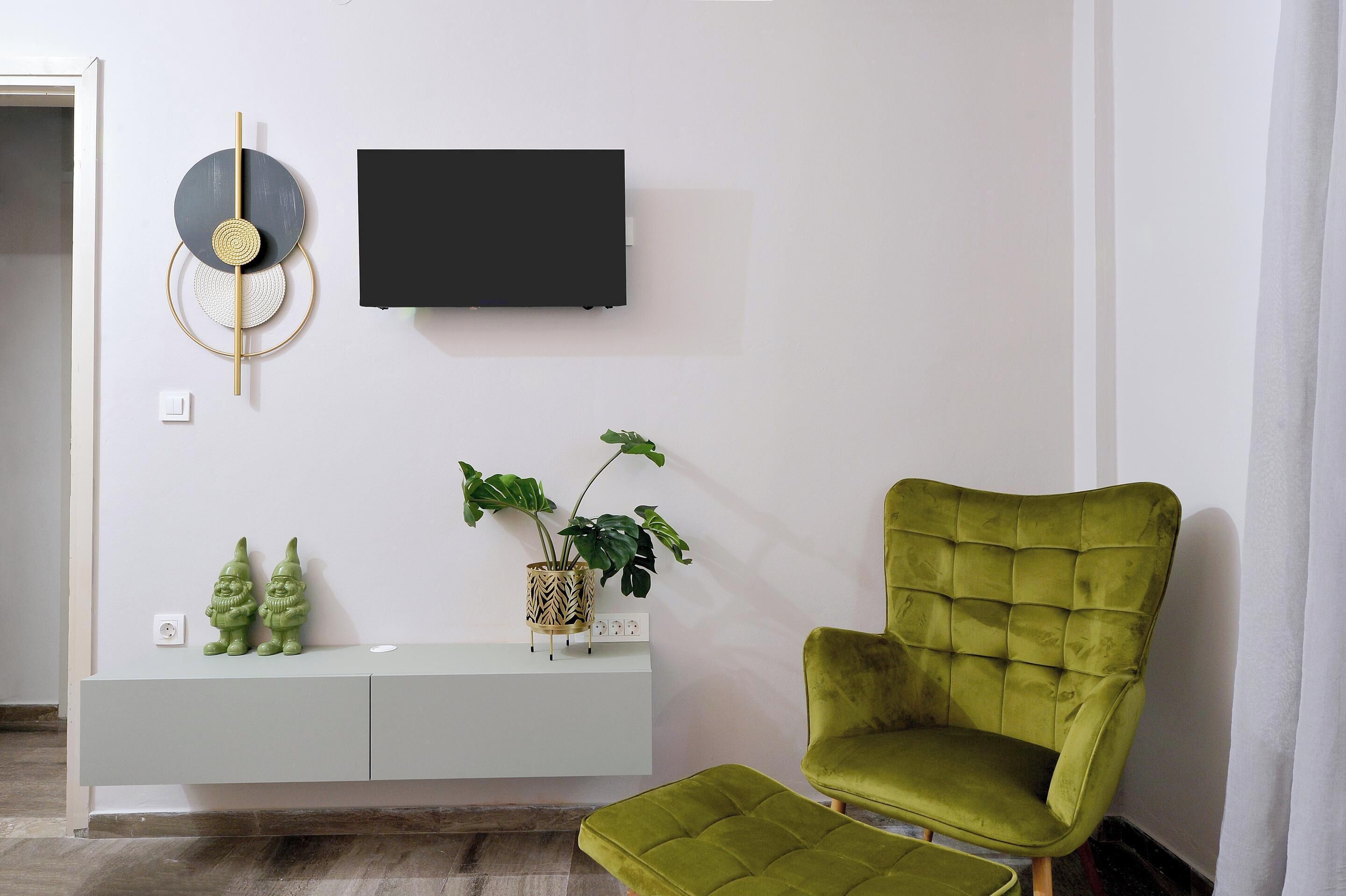A modern living room with a green armchair, a flat-screen TV, decorative wall art, and a small plant on a white console table.
