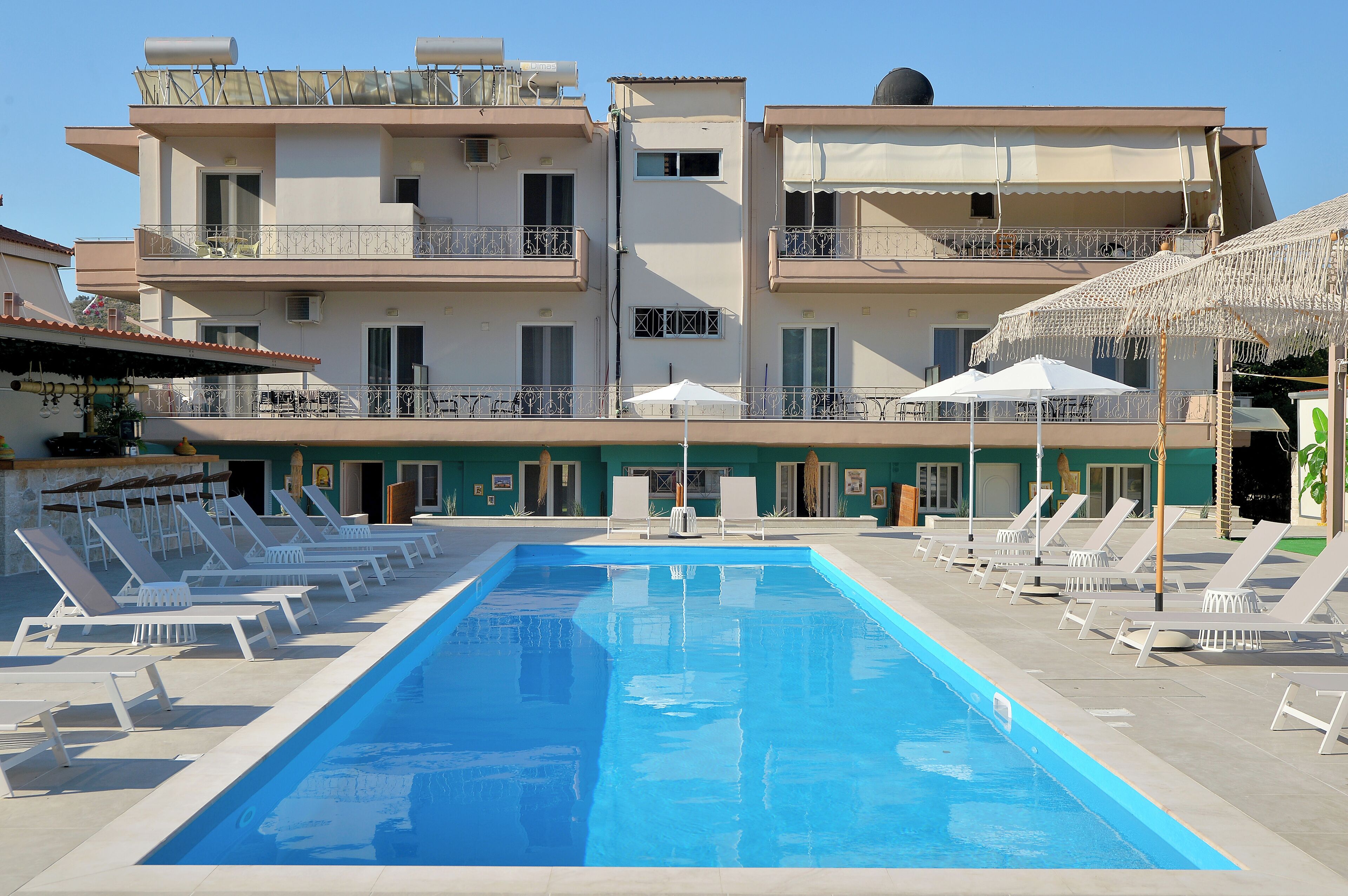 Una piscina con sillones de descanso y sombrillas, rodeada de edificios de varios pisos con balcones.