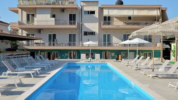 Una piscina con sillones de descanso y sombrillas, rodeada de edificios de varios pisos con balcones.