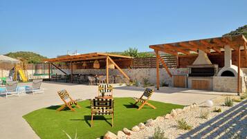 An outdoor patio area with a barbecue setup, seating, and a children's play area.