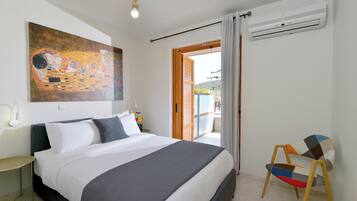 Un dormitorio con una cama grande, un cuadro en la pared, un equipo de aire acondicionado y vistas a través de una puerta abierta.