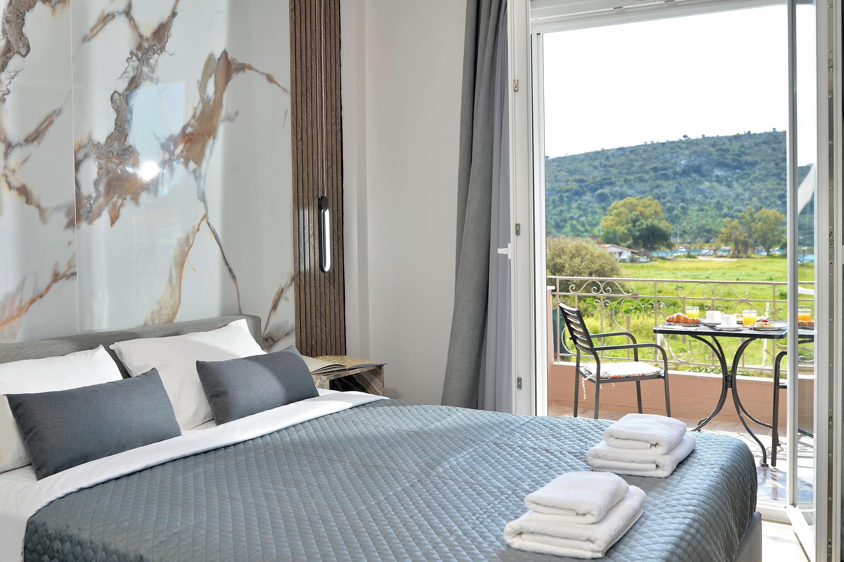 Un dormitorio con cama, almohadas, una mesita de noche y vistas a un balcón con mesa y sillas.