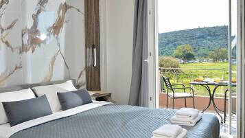 Un dormitorio con cama, almohadas, una mesita de noche y vistas a un balcón con mesa y sillas.