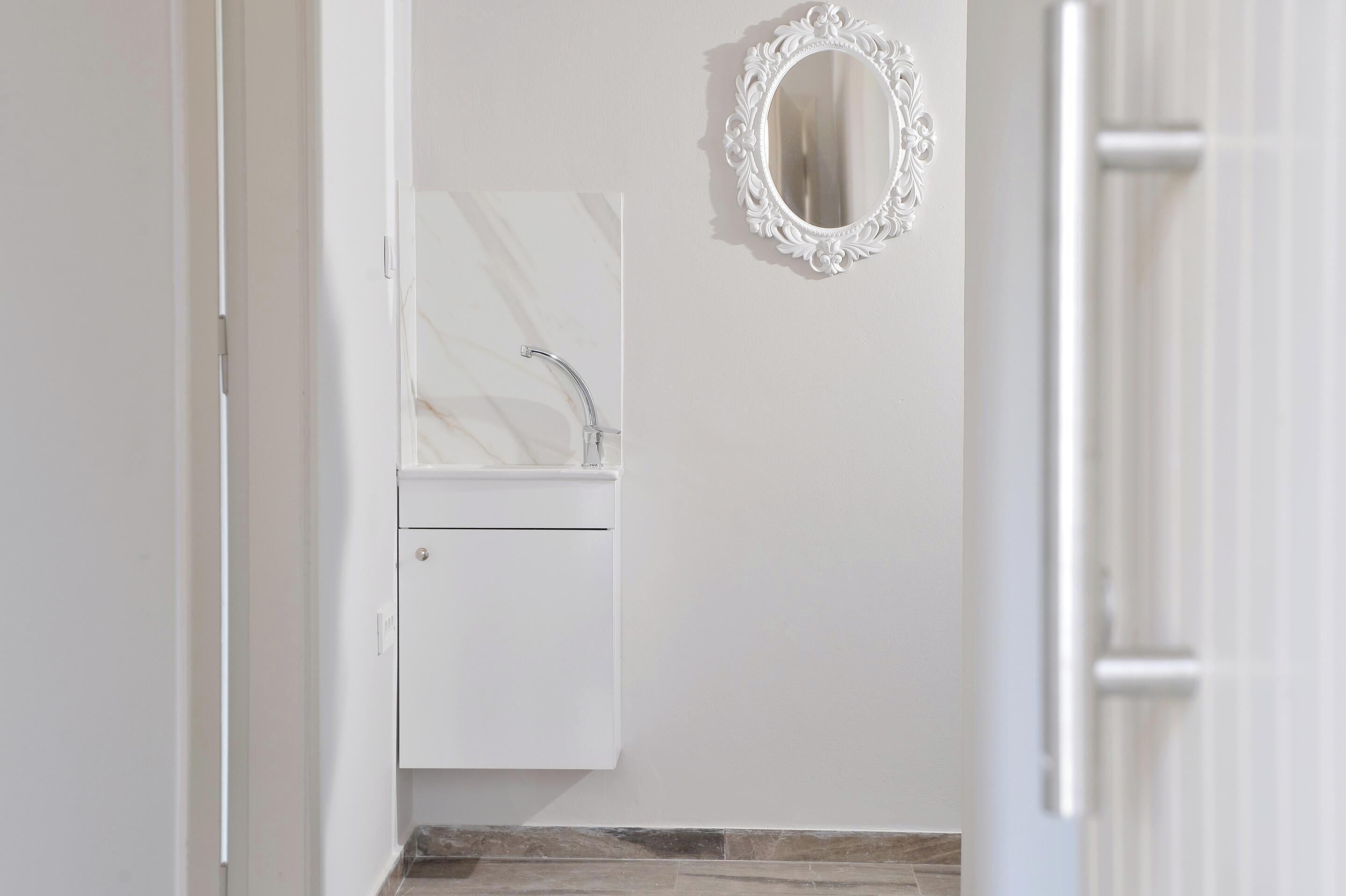 Un baño con lavamanos de mármol, un mueble pequeño y un espejo decorativo.