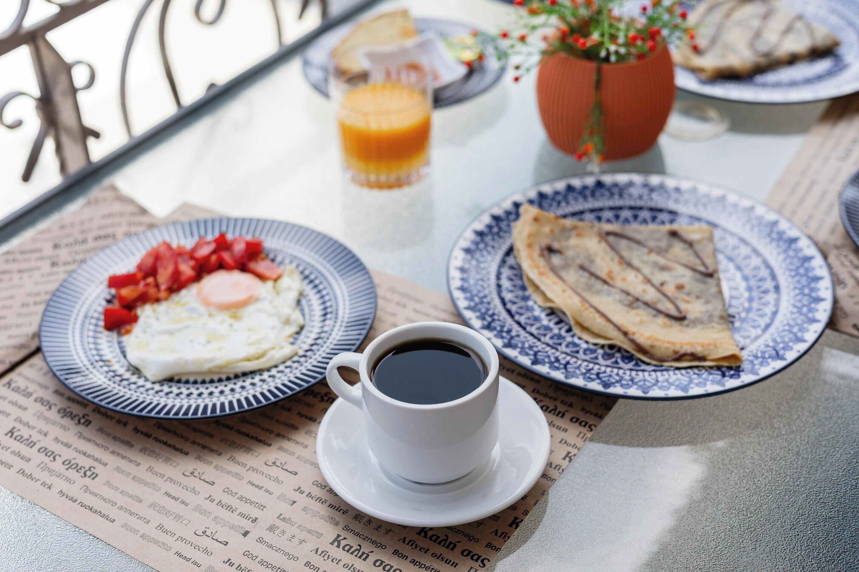 A breakfast table with plates of food, a cup of coffee, and a glass of orange juice.