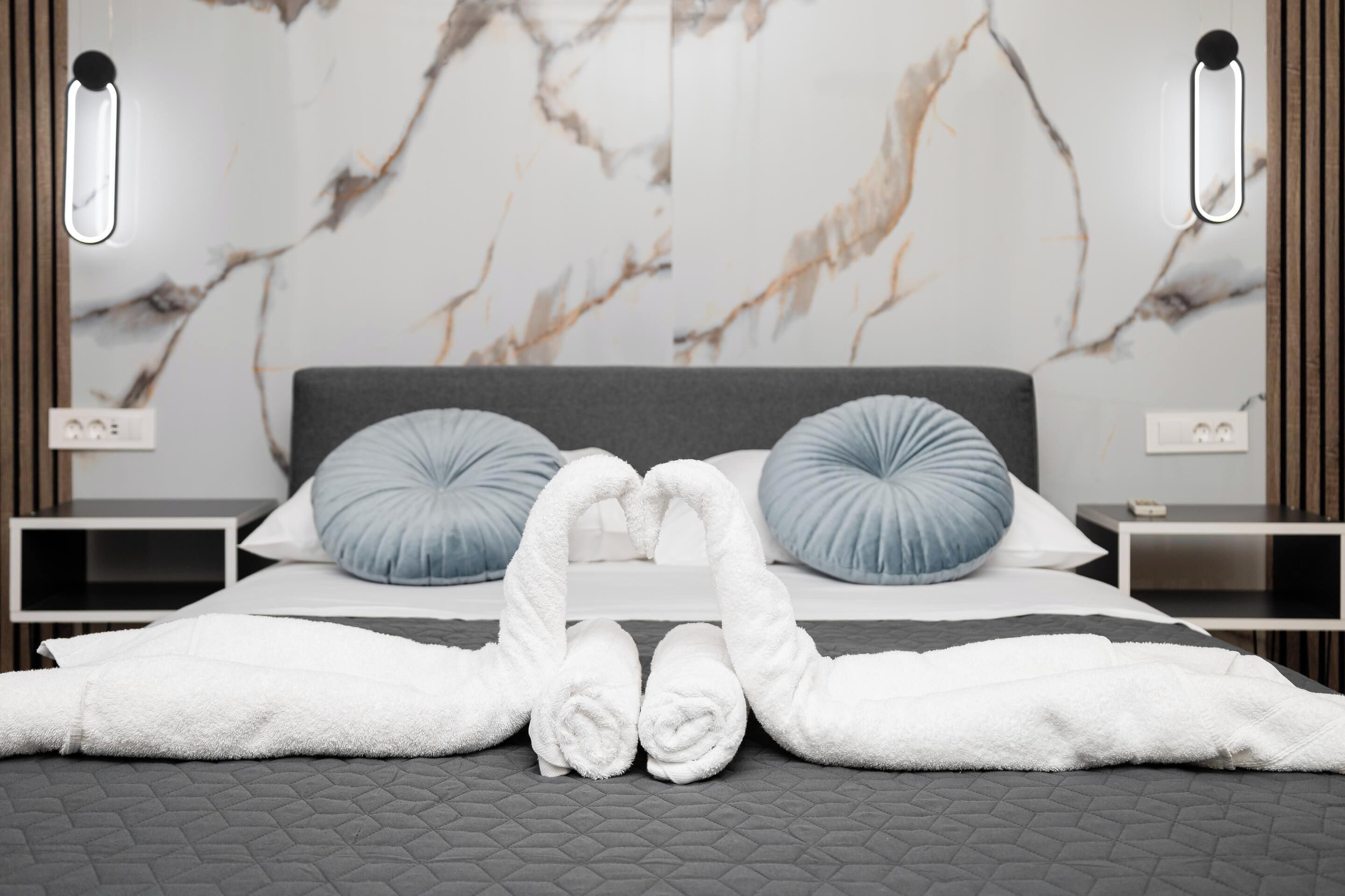 A bed with two pillows, a bedside table, and a wall with a marble pattern.