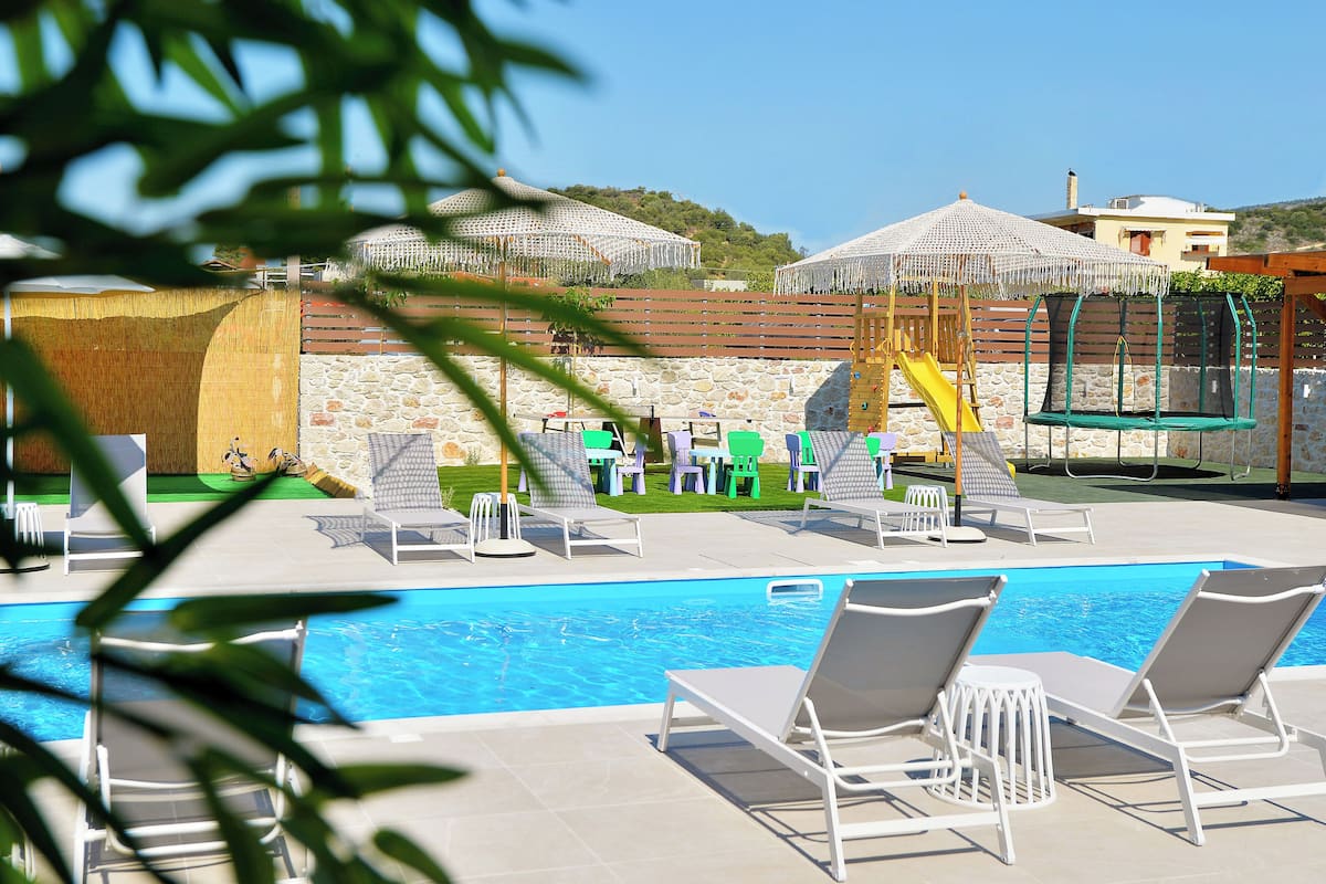 Un área de piscina con sillones de descanso, un tobogán y sombrillas.