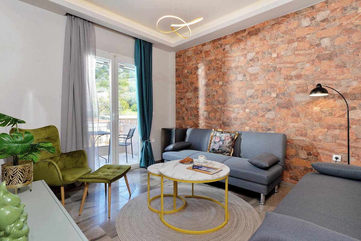 Una sala de estar moderna con una pared de piedra, un sofá gris, un sillón verde y una mesa de centro redonda.