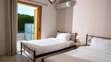 A bedroom with two beds, a small bedside table with a lamp, an air conditioning unit, and a sliding glass door leading to an outdoor area.