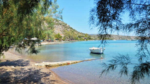 Un lago tranquillo con una barca, circondato da alberi e un pendio roccioso.