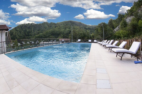 A swimming pool with lounge chairs and a view of a forested hill.