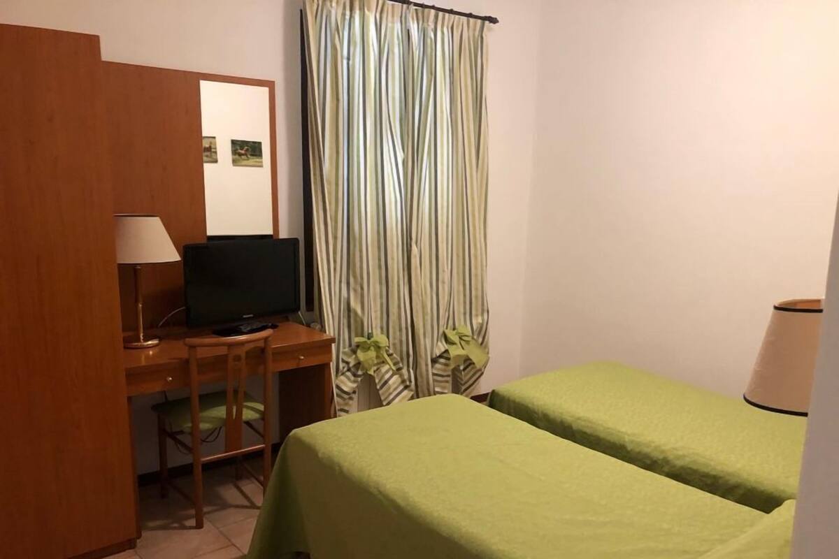 Een hotelkamer met een bureau, een televisie, twee eenpersoonsbedden, een gestreept gordijn en een lamp.