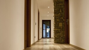 Un couloir doté d’un plancher en bois, de quelques éléments décoratifs en pierre et de portes en bois.