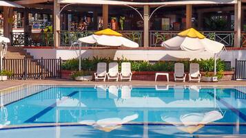 Piscina con sillones de descanso y sombrillas, rodeada por una valla y plantas en macetas.