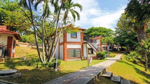 A bungalow-style house with a red-tiled roof, a small balcony, and a paved pathway leading to the entrance. - Hotel Girardot Resort by On Vacation (Ricaurte)