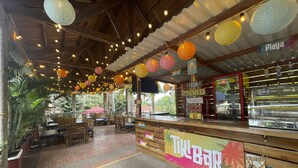 An outdoor bar area with wooden tables and benches, surrounded by tropical plants. - Hotel Girardot Resort by On Vacation (Ricaurte)