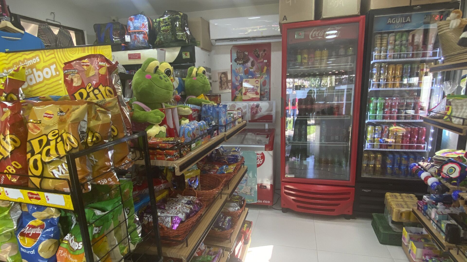 Una tienda de comestibles con pasillos de aperitivos, un refrigerador y un expositor de Coca-Cola.